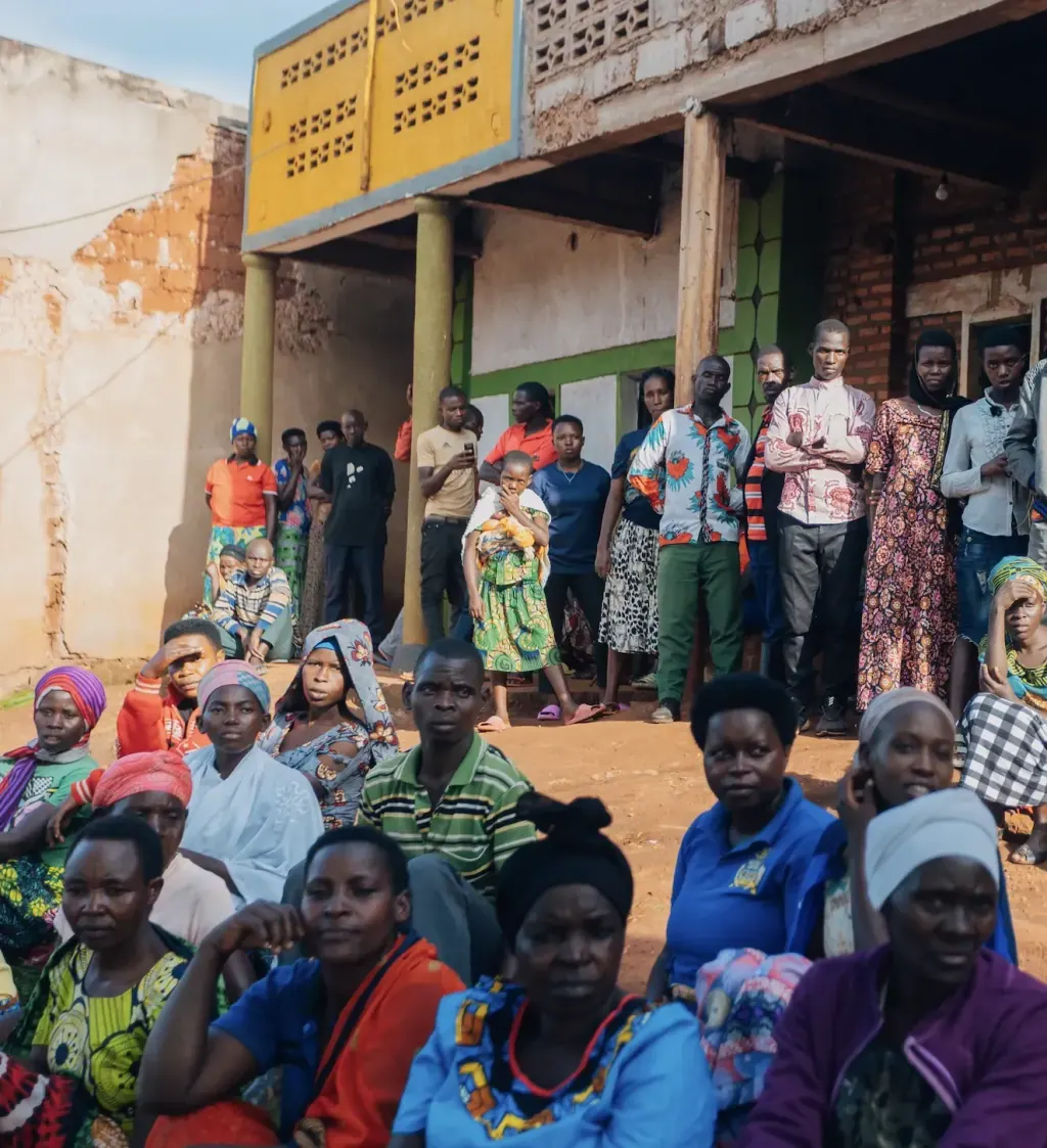 Village residents seated and standing together outdoors in front of a building during a Pink Village Movement gathering.
