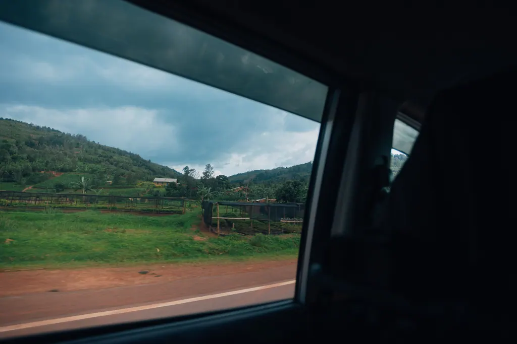 View through a car window onto a road and green hills.